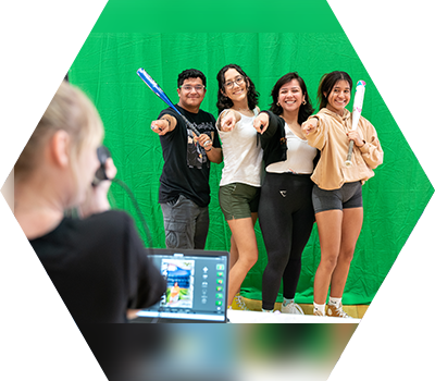 Students stand in front of green screen smiling with photographer taking their picture